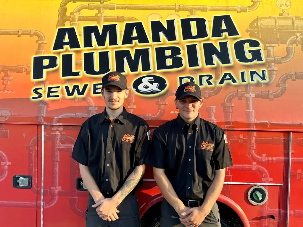 Two uniformed Amanda Plumbing technicians in front of a branded truck panel